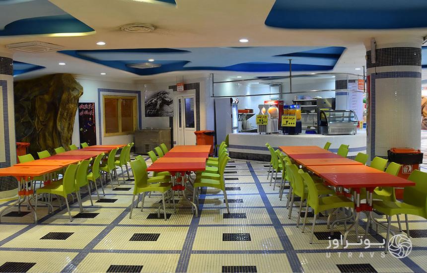 رستوران پارک موج‌های خروشان مشهد؛ با کفِ کاشی‌کاری‌شده، صندلی‌های سبز و میزهای قرمز و نارنجی
